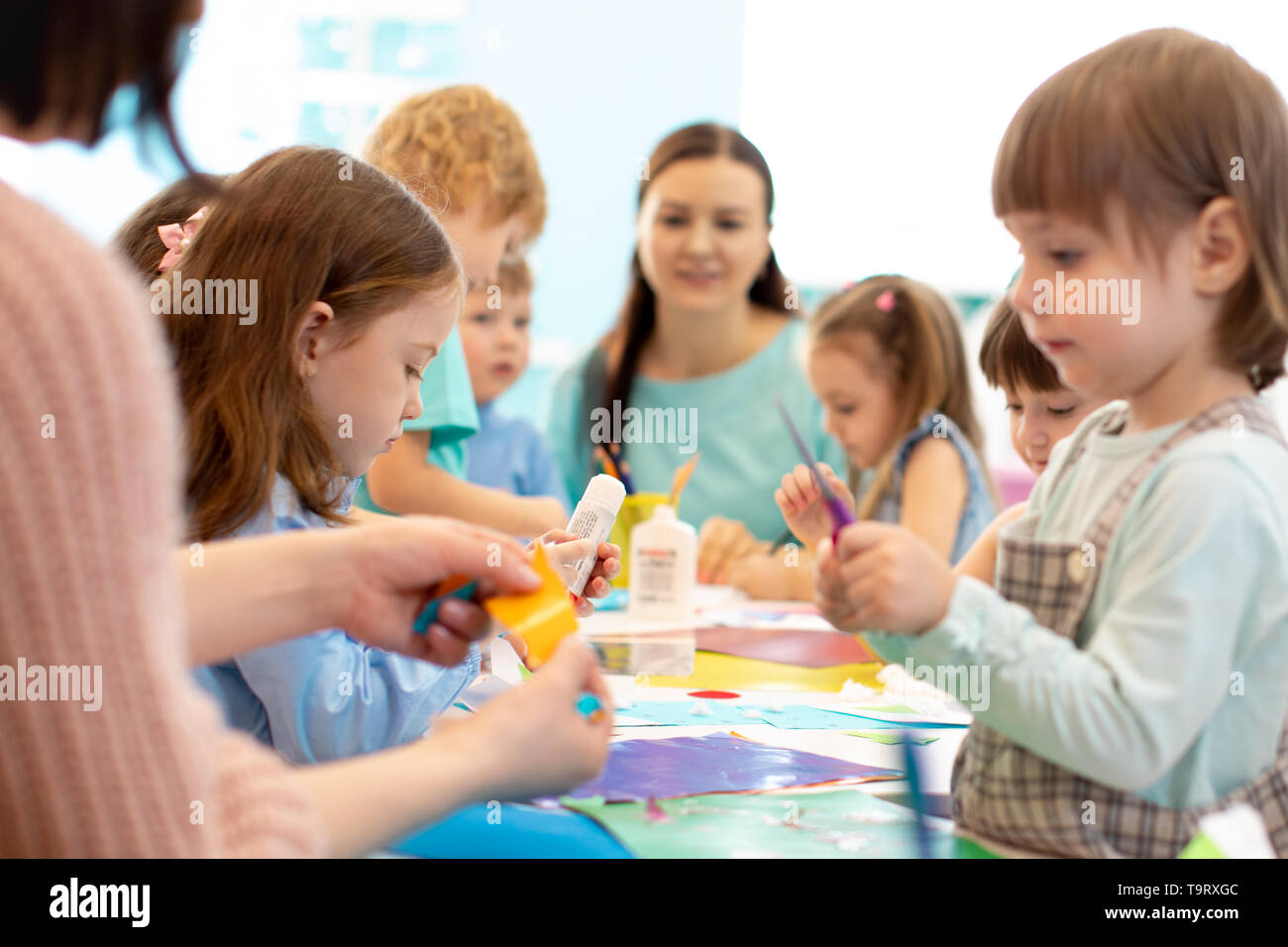 Development learning children in preschool. Children's project in kindergarten. Group of kids and teacher cutting paper and gluing with glue stick on art class in kindergarten or daycare Stock Photo