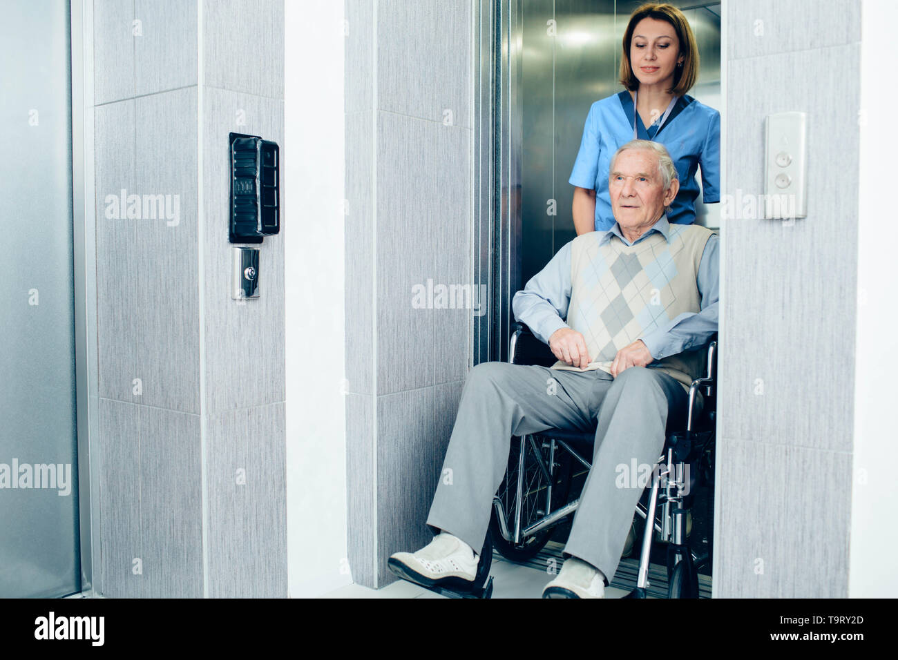 Thoughtful nurse pushing senior patient in wheelchair at hospital lift Stock Photo