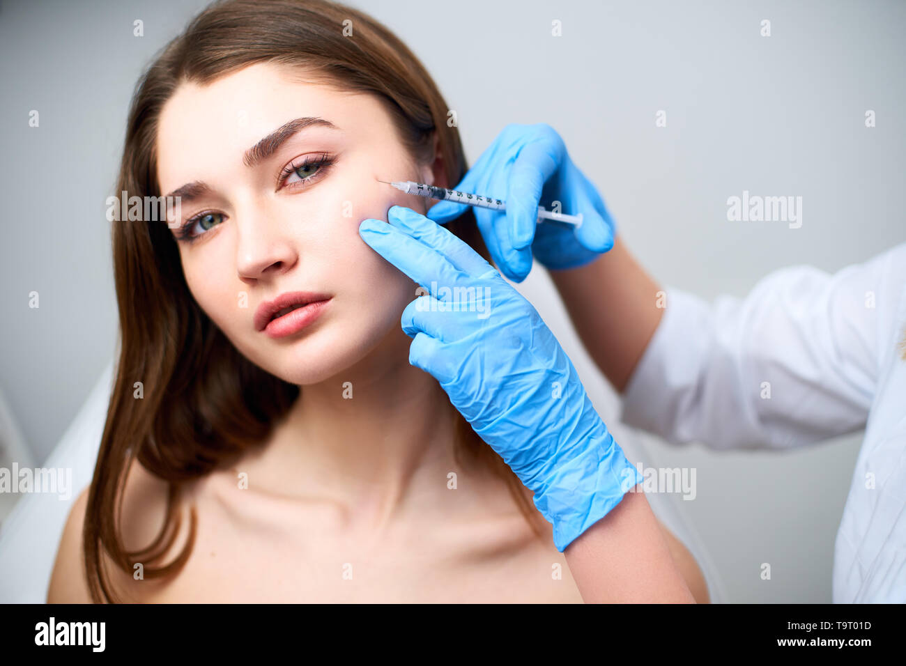 Beautician doctor with botulinum toxin syringe making injection to to remove crow's feet. Cheek volume enhance mesotherapy. Anti-aging treatment and Stock Photo