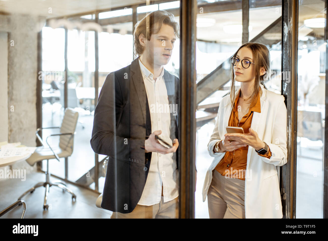 Business man and woman having a conversation while standing together with smart phones in the modern office Stock Photo