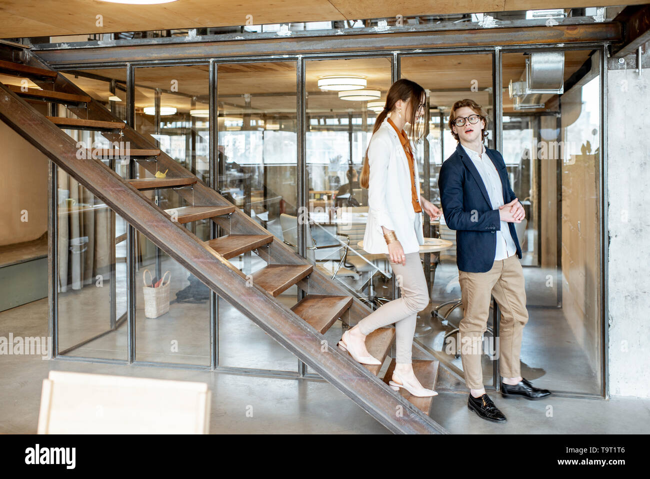 Business man and woman walking down the stairs in the hall of the modern office or coworking space Stock Photo