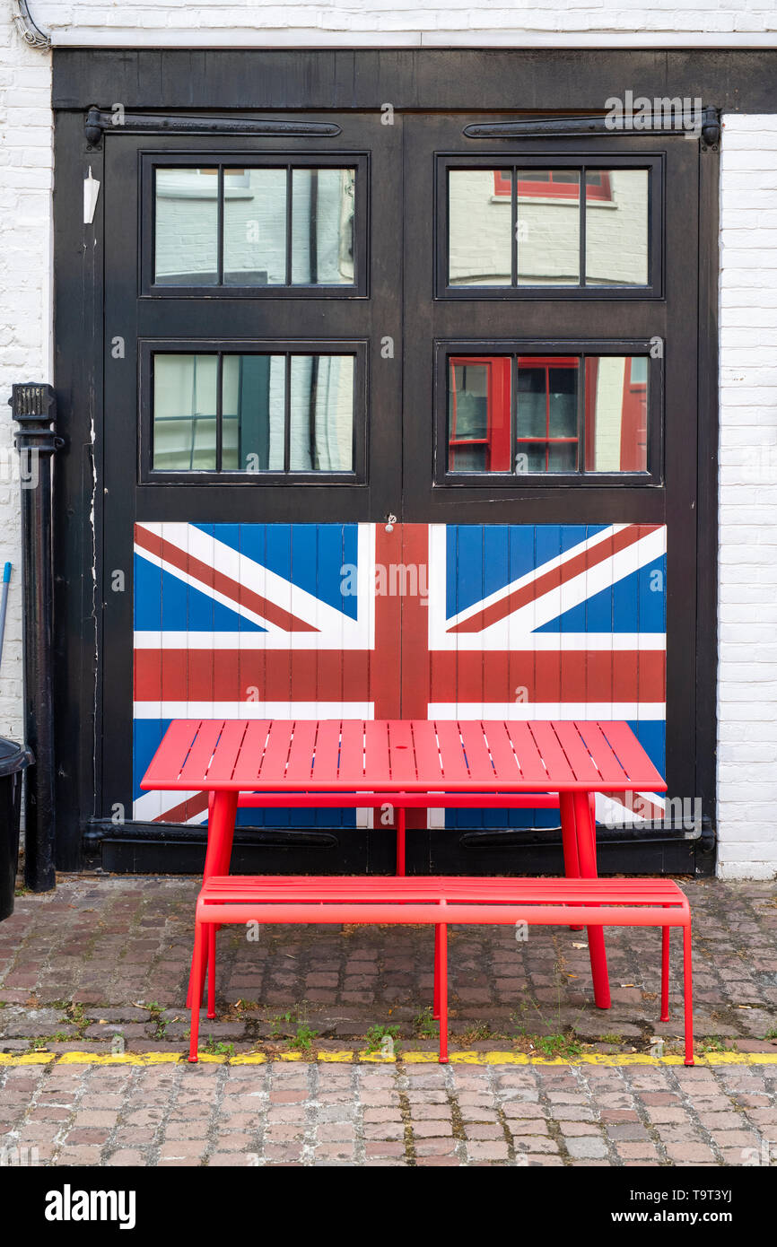 Red table in front of a lion jack painted on black garage doors in Cranley mews , South Kensington, SW7, London. England Stock Photo