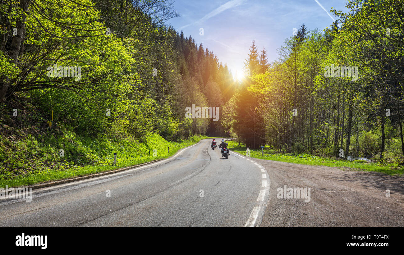 Bikers on mountainous highway, biker on the road in sunset light riding on curve road pass across Alpine mountains, extreme lifestyle, freedom concept Stock Photo