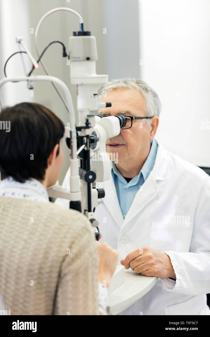 Senior male ophthalmologist determines diopter to patient using ophthalmoscope Stock Photo