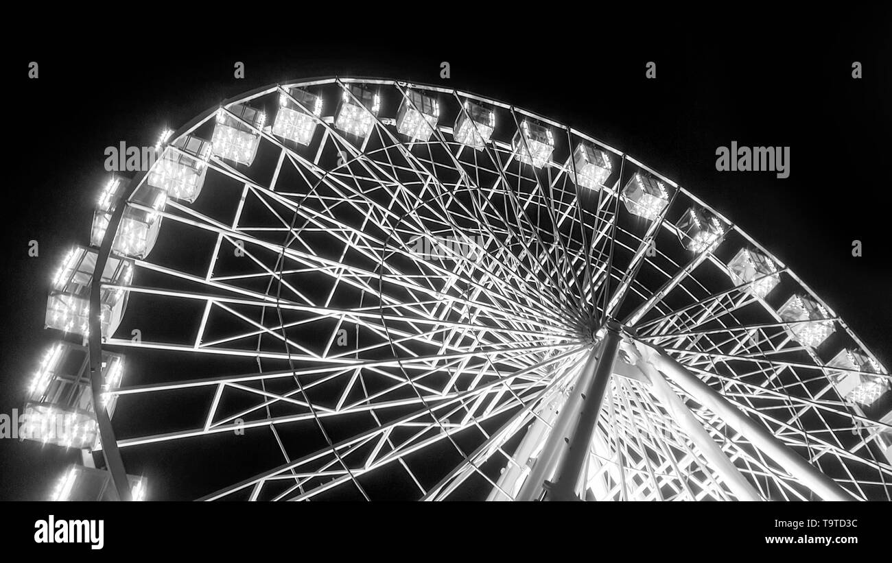 Black and white image of rotating illuminated ferris wheel in amusement