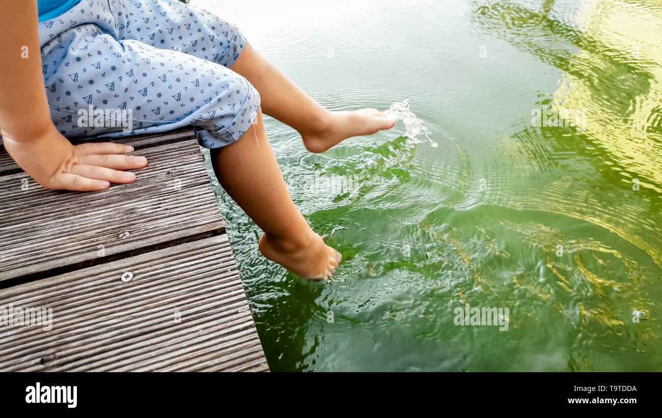 Closeup image of child sitting on the wooden pier at tiver and holding