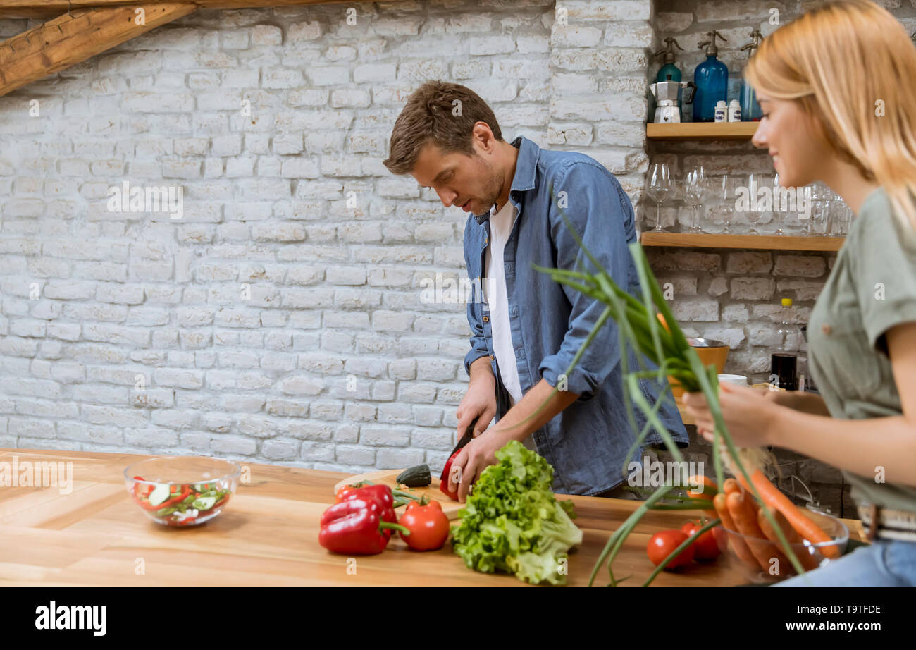 Trendy couple peeling and cutting vegetables from the market in rustic kitchen Stock Photo