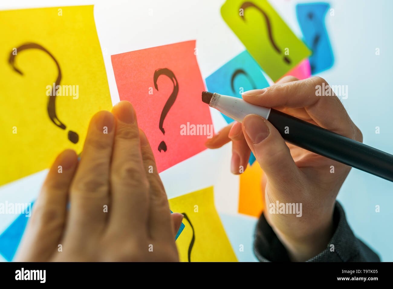 Businesswoman writing question marks on colorful sticky note paper on office whiteboard, selective focus Stock Photo