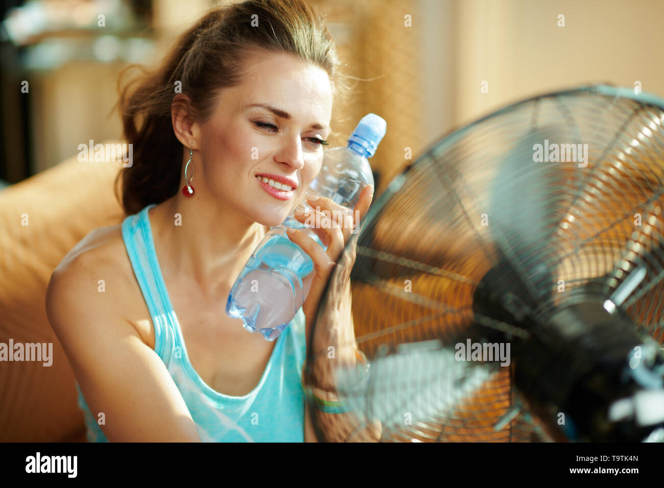 hot woman with bottle of cold water using electric metallic fan at
