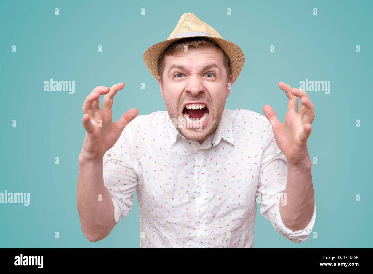 Furious,enraged man with mouth opened in shout, show level of his anger, isolated over blue background Stock Photo