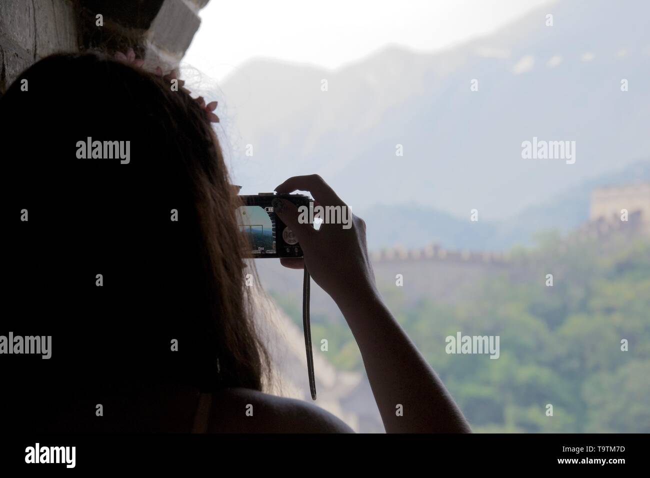 Silhouette of lady taking a photograph of the Great Wall of China, the wall visible through her camera. Stock Photo