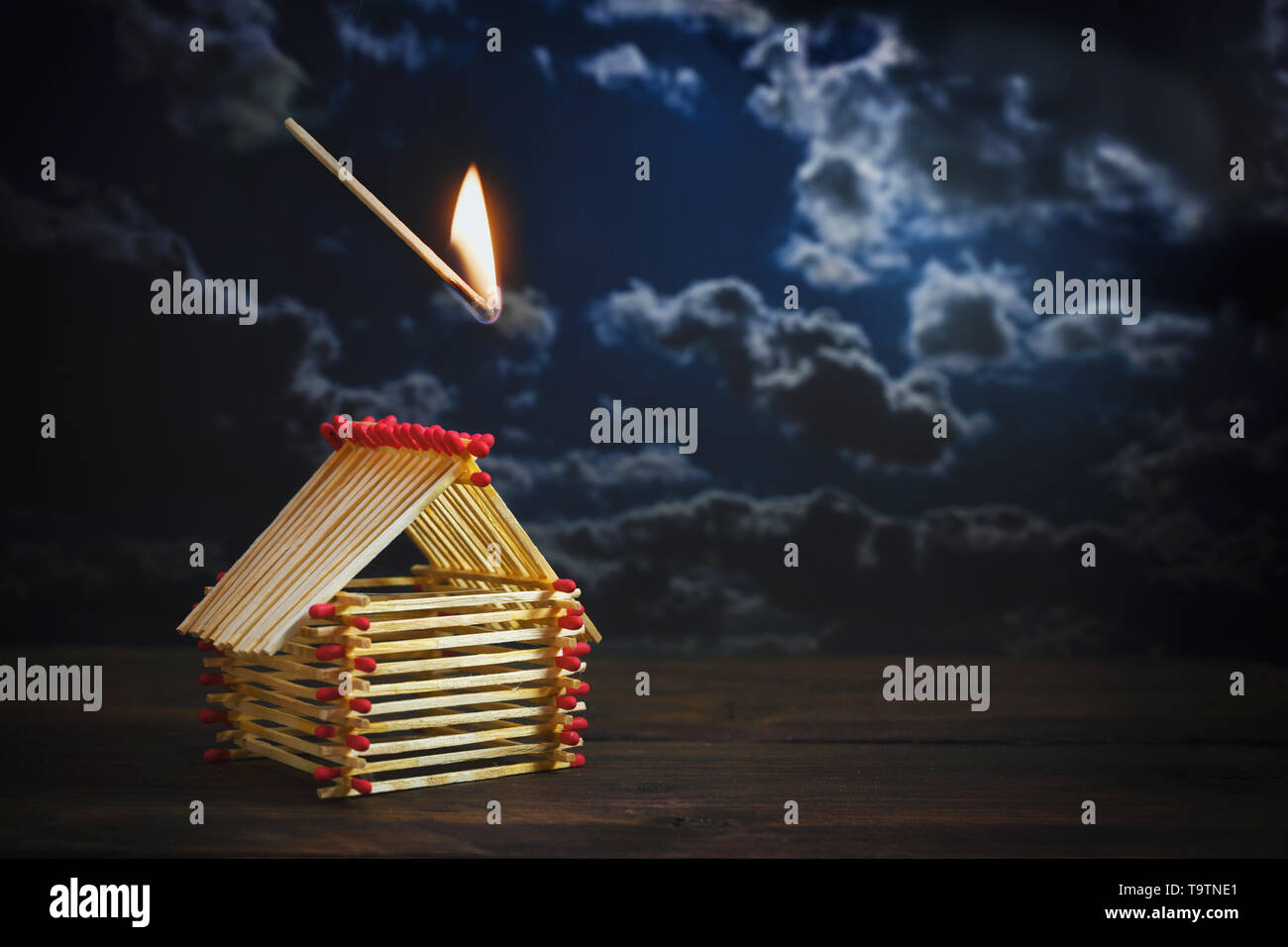 inflamed match is falling on a house built of matches against a dark stormy sky with copy space, insurance concept for danger or financial  risk in re Stock Photo