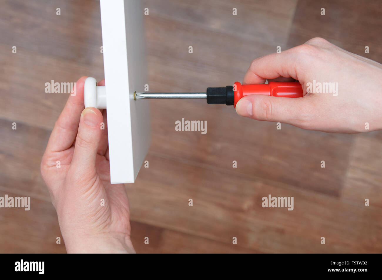 Furniture assembly. Hands of the girl close up. A screwdriver fastens the white knob to the cabinet door. Stock Photo