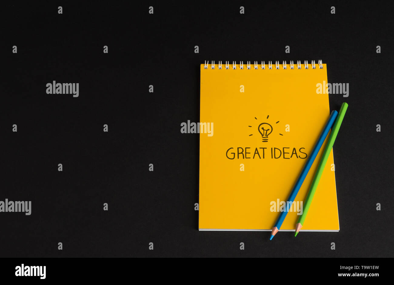 yellow notepad with colored pencils on black background, isolated. back to school. great ideas Stock Photo