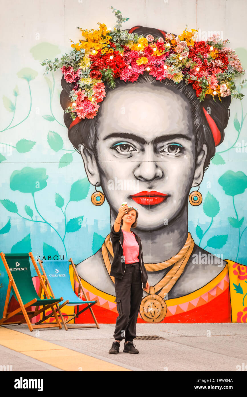 Belgravia, London, UK, 20th May 2019. A young woman takes selfies with an existing installation by Moyses Stevens florial artistry, which is again on display with other new floral displays in Eccleston Yards. The work shows a floral crown above a painting of Frida Kahlo by artist Zabou, called 'Frida with Flowers' (in situ since 2018).  Belgravia's fourth annual floral festival coincides with the RHS Chelsea Flower Show in neighbouring Chelsea. Credit: Imageplotter/Alamy Live News Stock Photo
