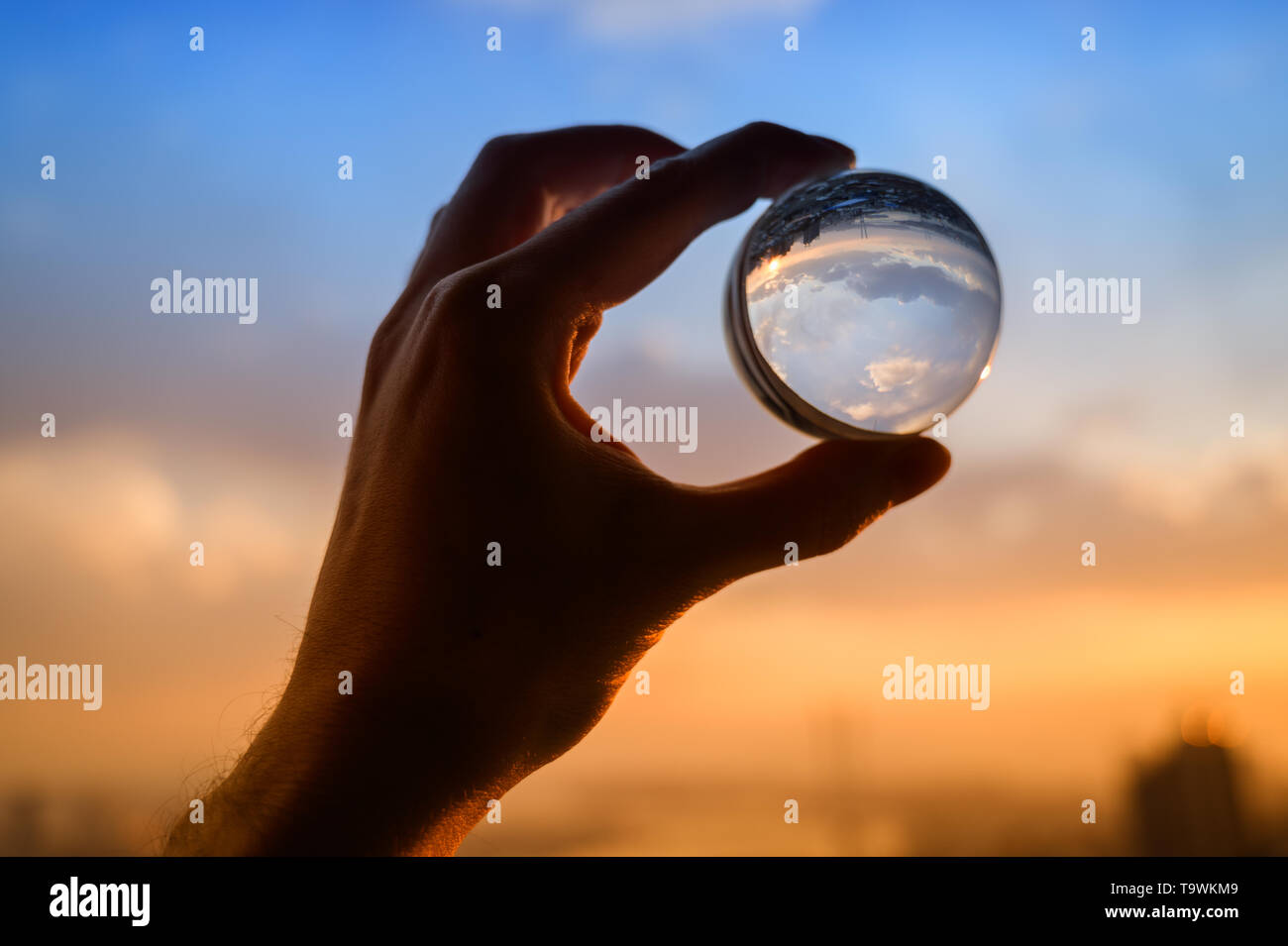 The hand holds glass ball which reflects sunset sky over city Stock ...