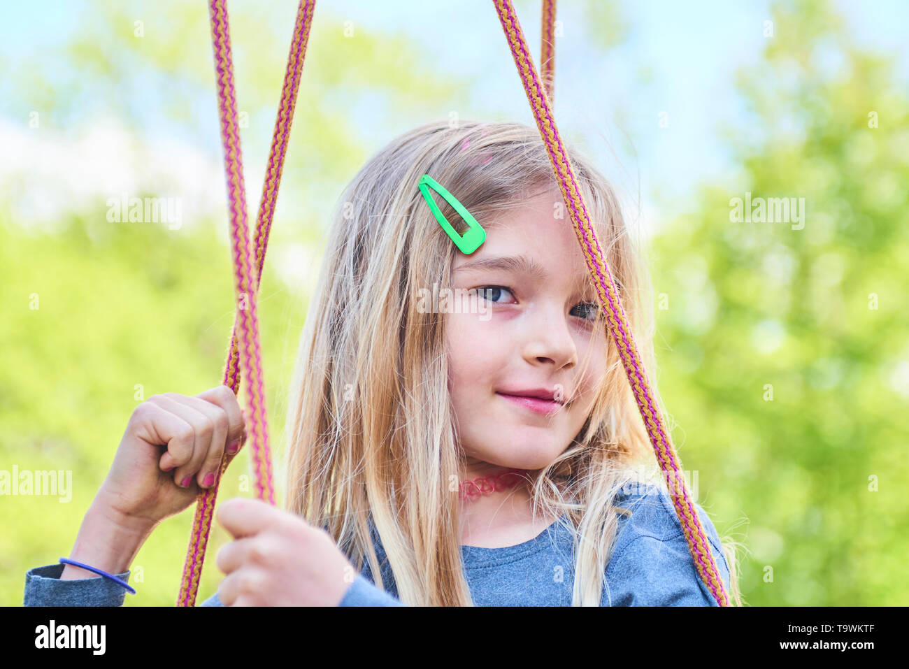 Portrait of little cute blond girl with blue eyes swinging. Close up ...