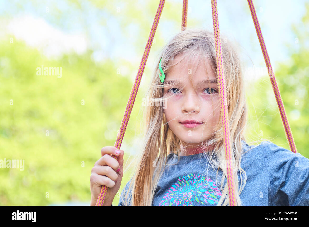Portrait of little cute blond girl with blue eyes swinging. Close up ...