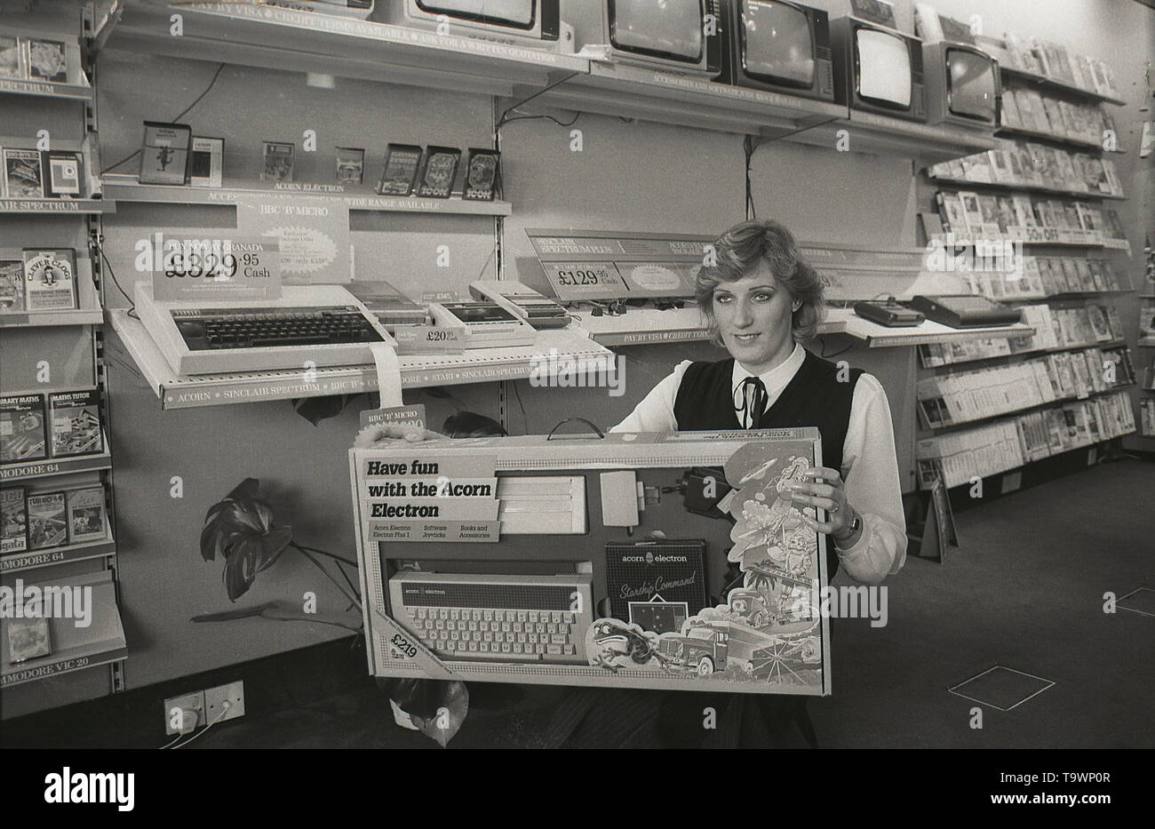 1985, historical, home entertainment equipment inside a Granada TV retail shop, a female shop assistant shows a box containing the new Acorn Electron home computer, England, UK. Stock Photo