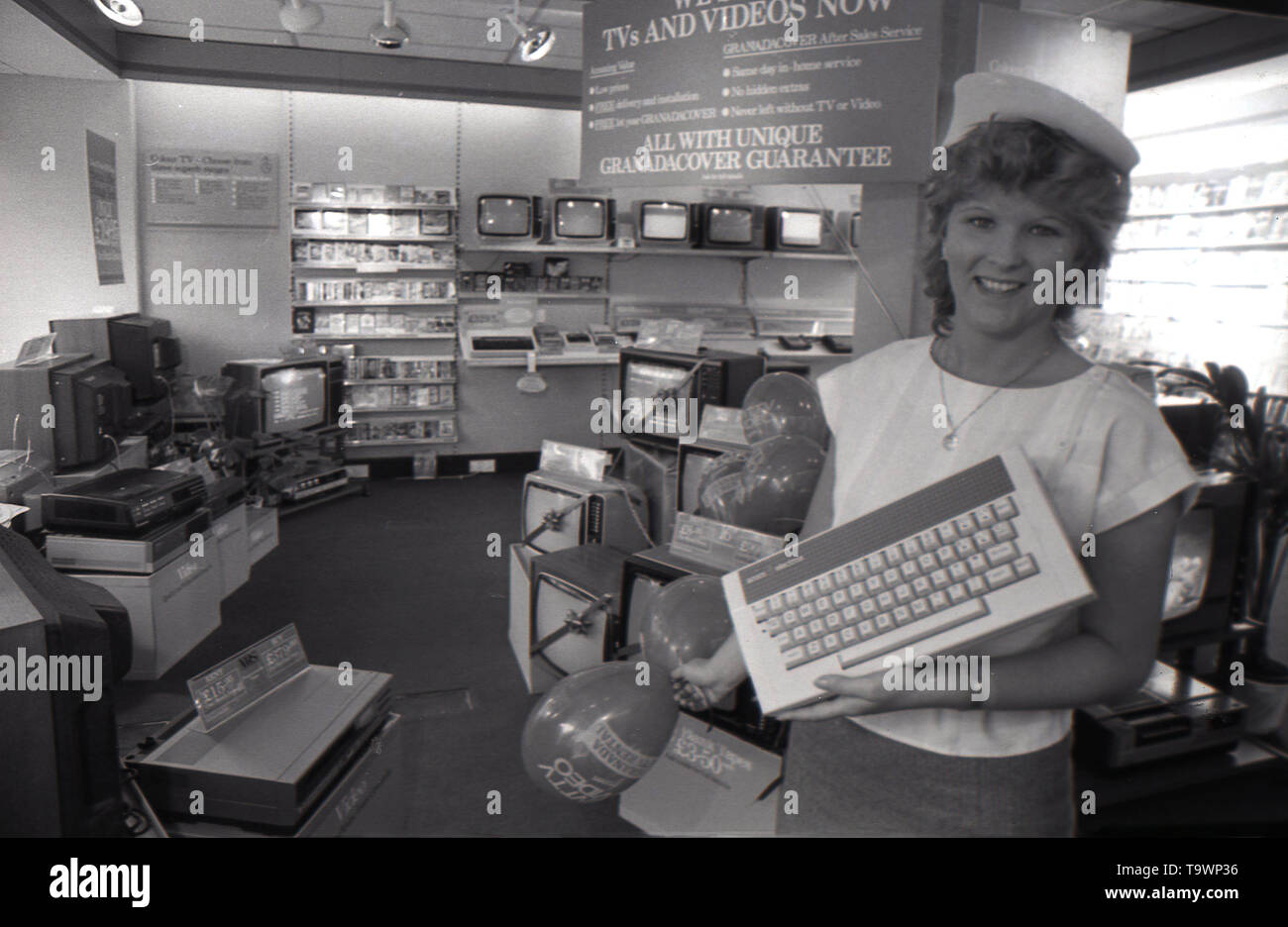 1985, historical, home entertainment equipment inside a Granada TV Rental shop, picture shows a female shop assistant holding a keyboard for a new piece of electronic equipment, the home computer, England, UK. Stock Photo