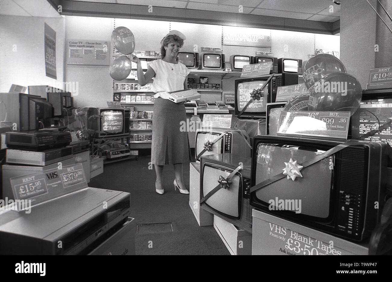 1985, historical, home entertainment equipment inside a Granada TV Rental shop, a female shop assistant holds a new 'home computer together with some ballons, England, UK. Stock Photo