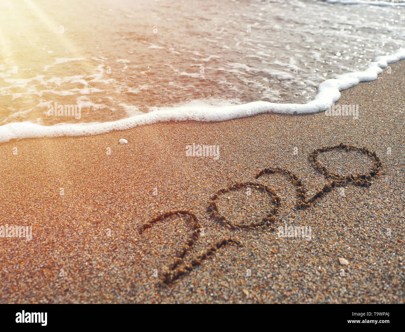 Year 2020 Hand Written On Sandy Beach In Sunset Warm Lens Flare