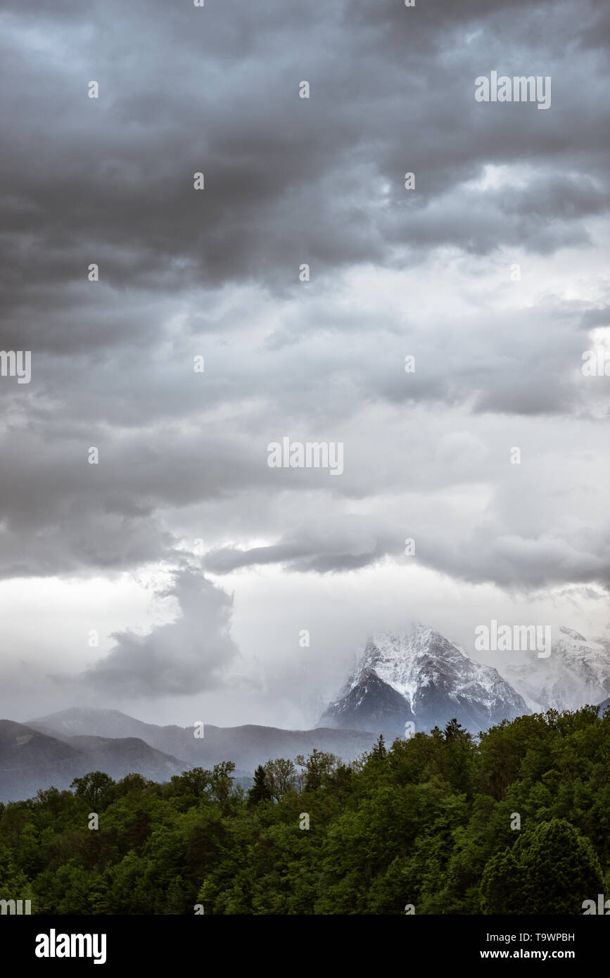Landscape image of cloudy sky over snowy mountains and green forest in ...