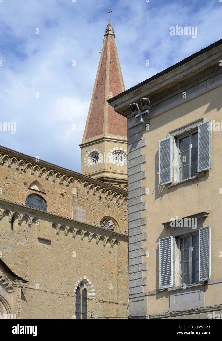 urban view of Arezzo historic center with an ancient building facade and the Cathedral in the background, under the cloudy and sunny sky Stock Photo