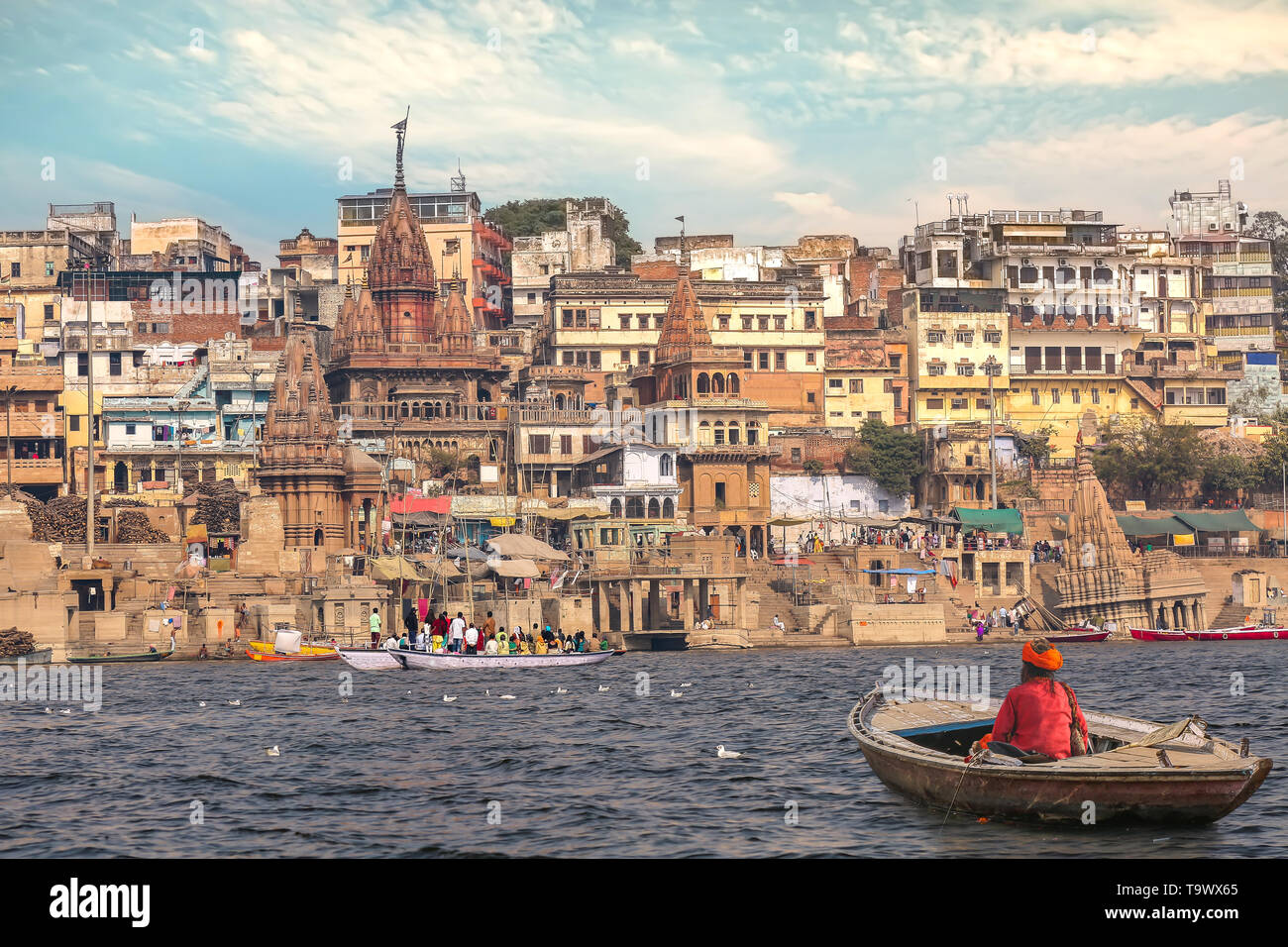 Aged man sitting on a wooden boat on river Ganges overlooking the historic Varanasi India city architecture at sunset Stock Photo