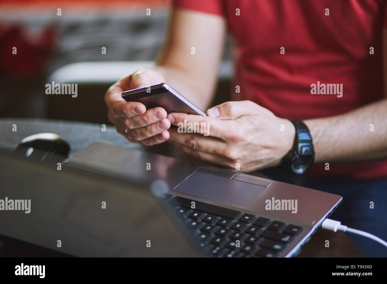 Man using smartphone working on laptop sitting at a desk Stock Photo