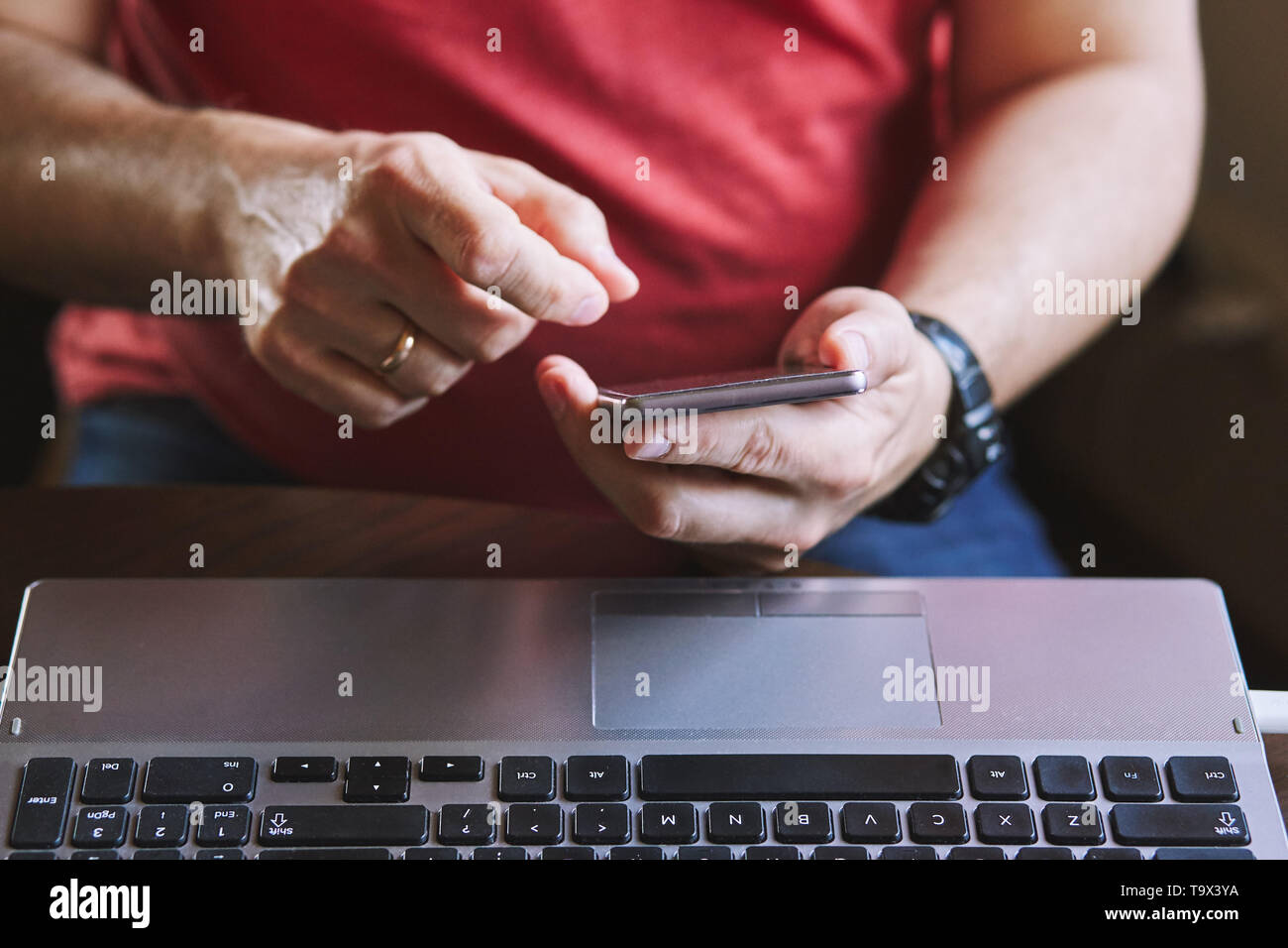 Man using smartphone working on laptop sitting at a desk Stock Photo