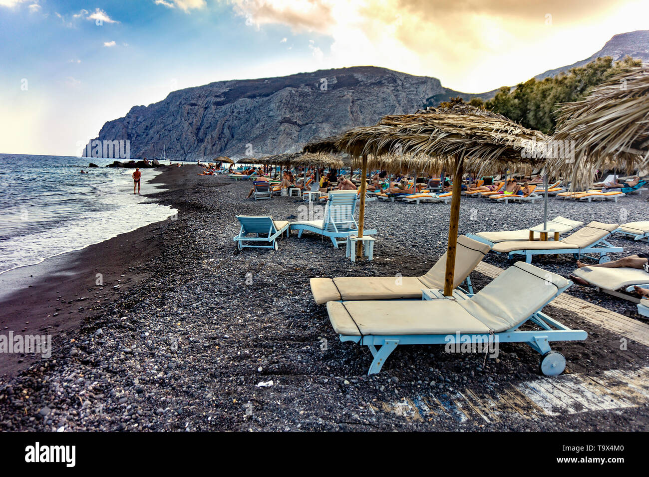 Oia, Santorini / Greece - 09.05.2018: Sunbeds at Kamari beach Santorini with a big rock in the background Stock Photo