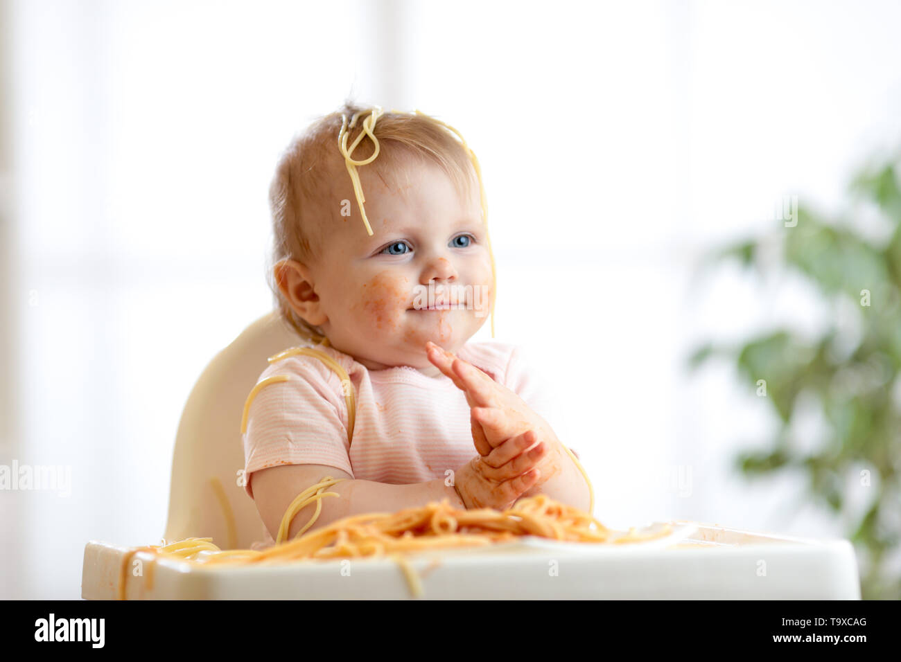 Funny baby eating noodle. Grimy child eats spaghetti with hands sitting