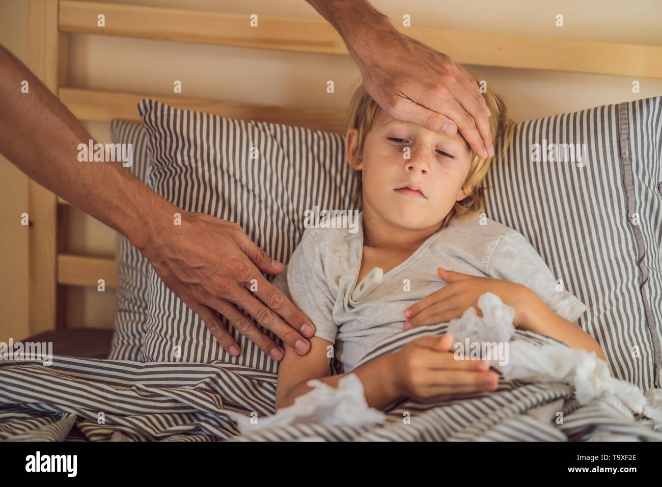 Sick boy with thermometer laying in bed and father hand taking