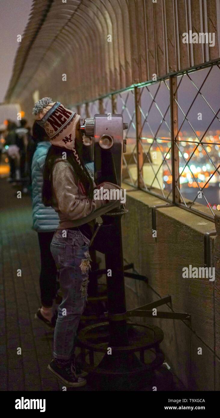 A teenage girl looking through coin-operated binoculars from atop the Empire State Building in New York City. Stock Photo