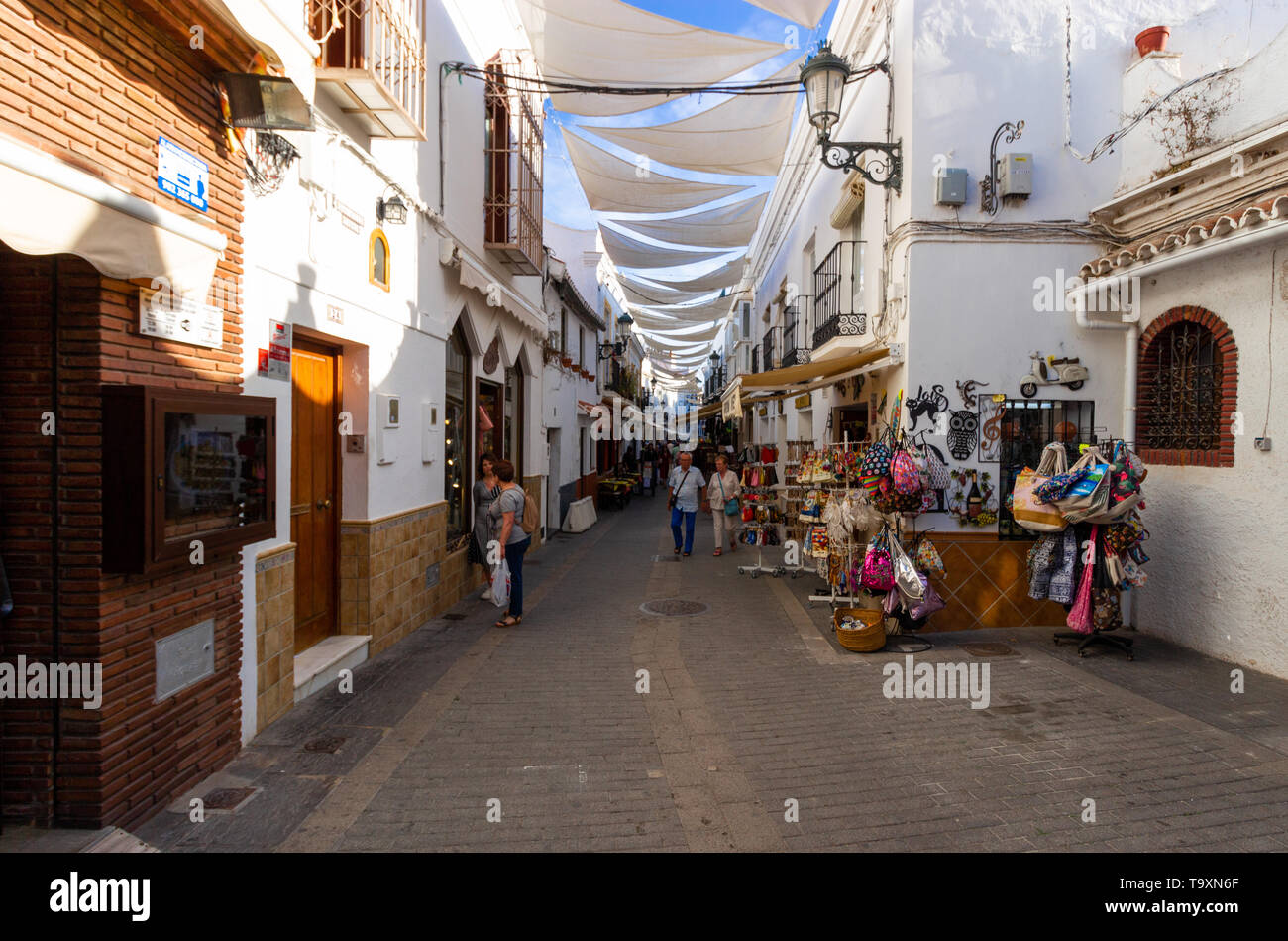 Nerja, Malaga, Andalusia, Spain, May 18 2019. A tradition narrow shopping street with shades high up between the buildings to block the sunlight Stock Photo