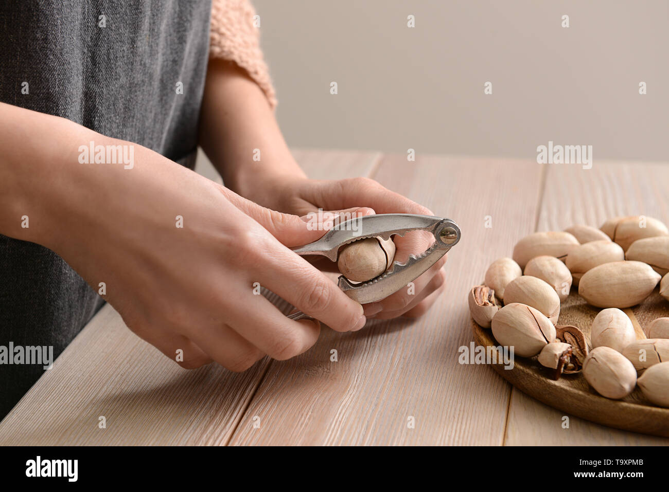 Woman cracking pecan nuts at wooden table, closeup Stock Photo
