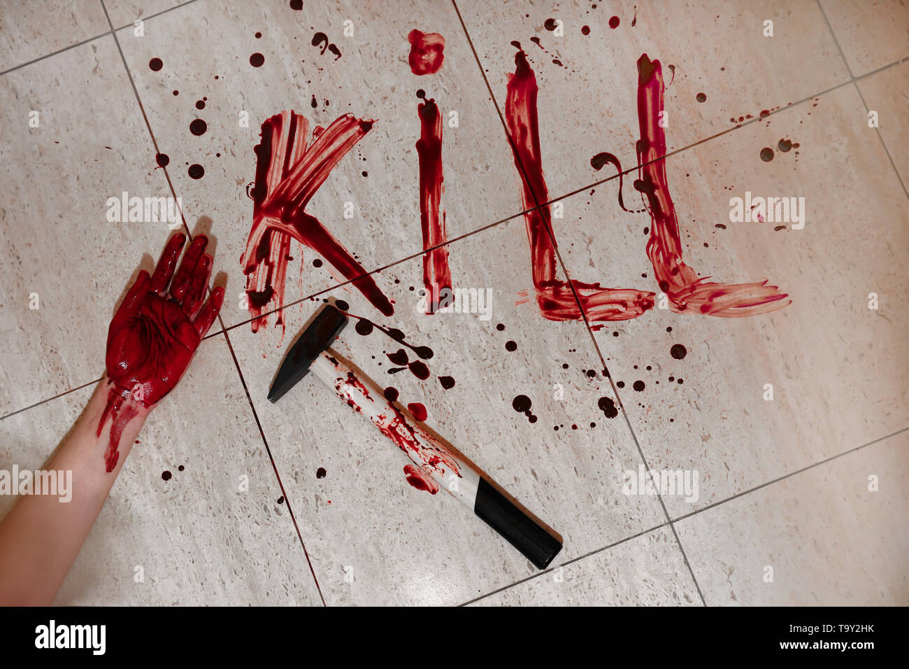 Hand of victim with word KILL written in blood and hammer on floor Stock Photo