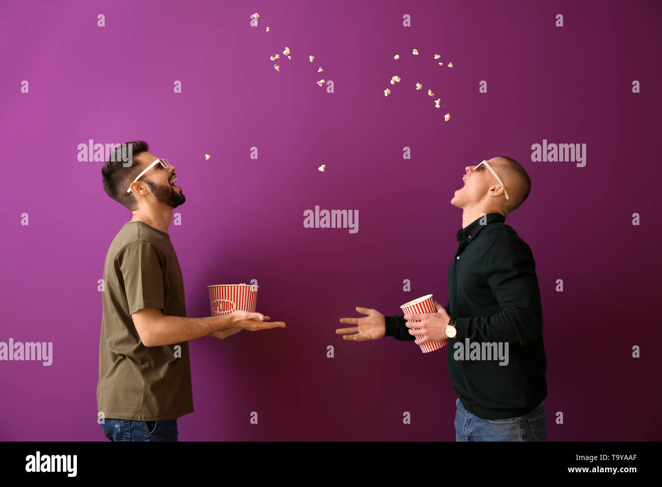 Guys catching popcorn with their mouths on color background Stock Photo ...