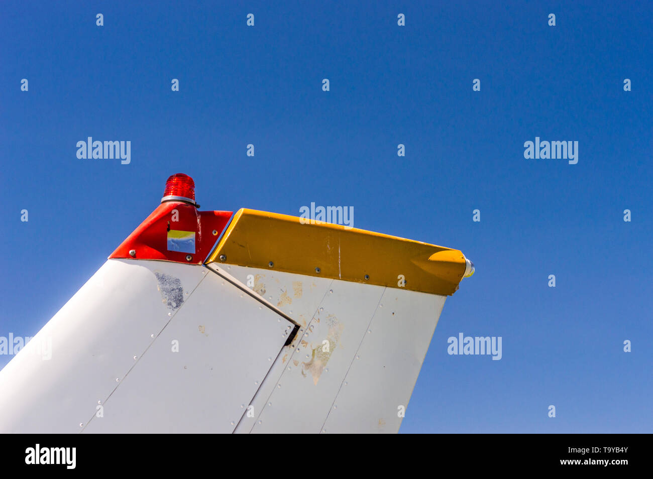 Tail fin, rudder and beacon lights, small single engine airplane with old paint and bright blue sky on sunny day. Stock Photo