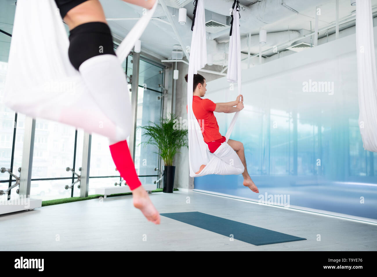 Man wearing t-shirt practicing aerial yoga attending group classes Stock Photo