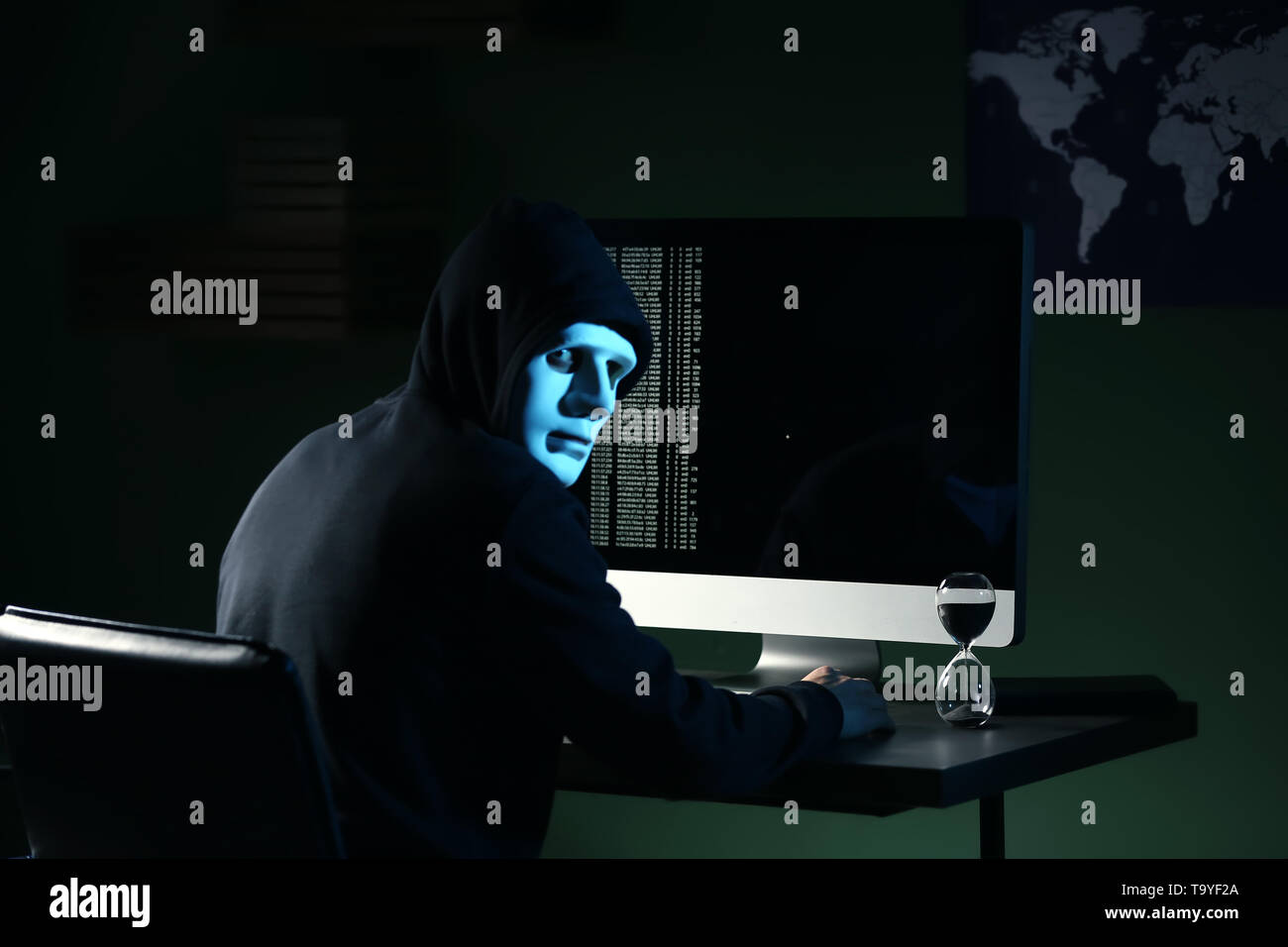 Professional hacker in mask using computer in dark room Stock Photo