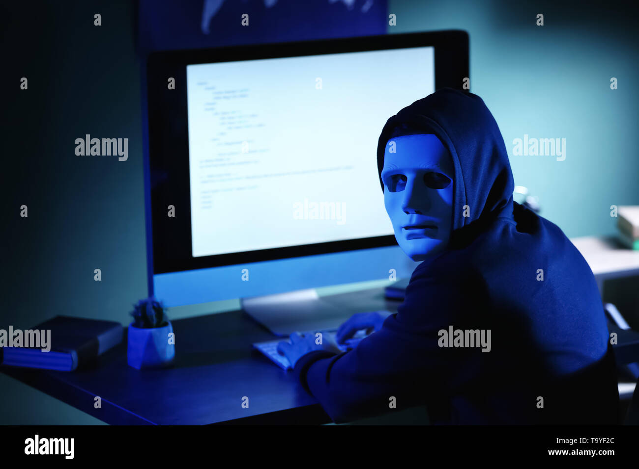 Professional hacker in mask using computer in dark room Stock Photo