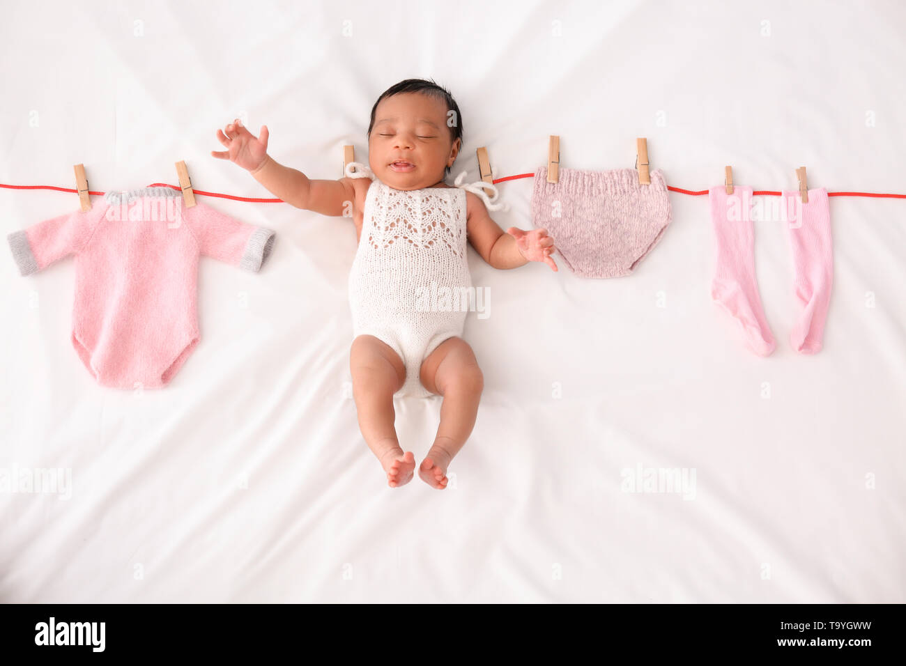 Cute AfricanAmerican baby with clothes on rope lying on white blanket