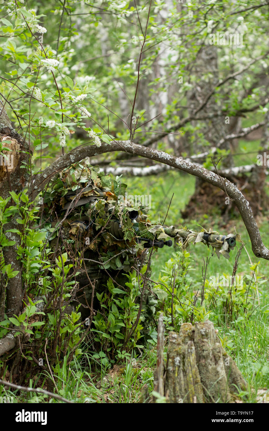 Nice green camouflage clothing military man in ambush in the woods. Sniper aiming rifle, machine gun, waiting for the enemy in nature Stock Photo