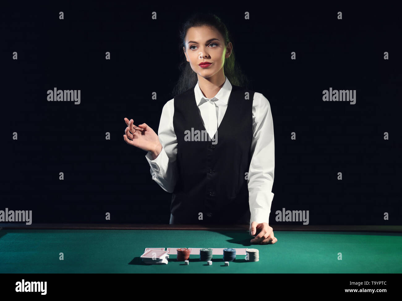 Woman croupier near card table in casino offers to play black jack