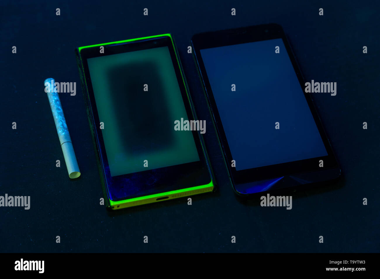 used phones and cigarette under UV light on black bckground with