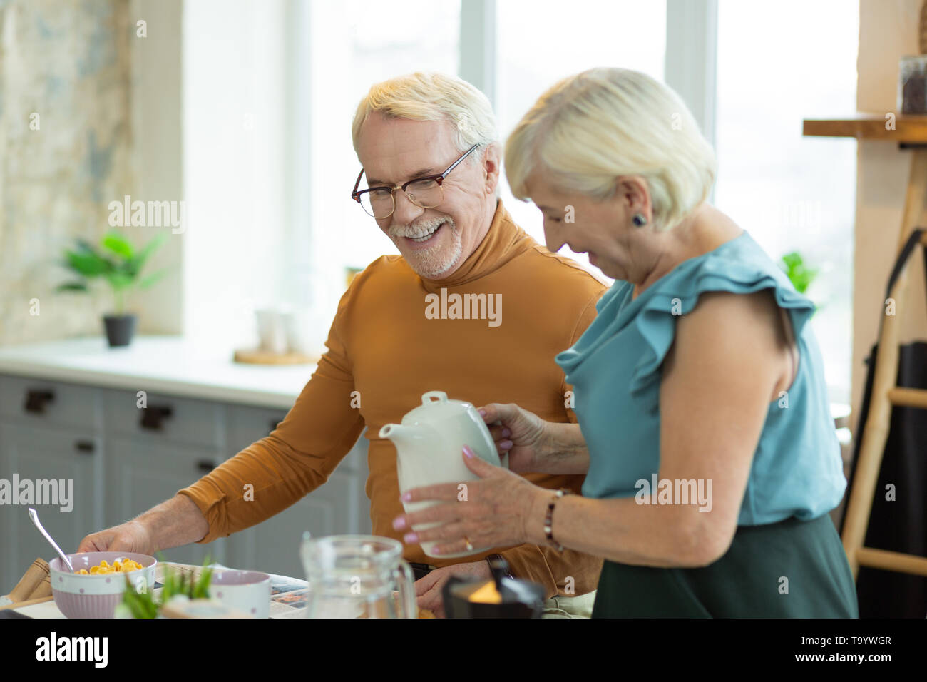 Kind lady pouring tea for her silver-haired attractive nice-looking spouse Stock Photo