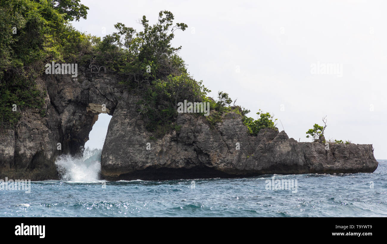 island with hole in a cliff and waves coming through Stock Photo