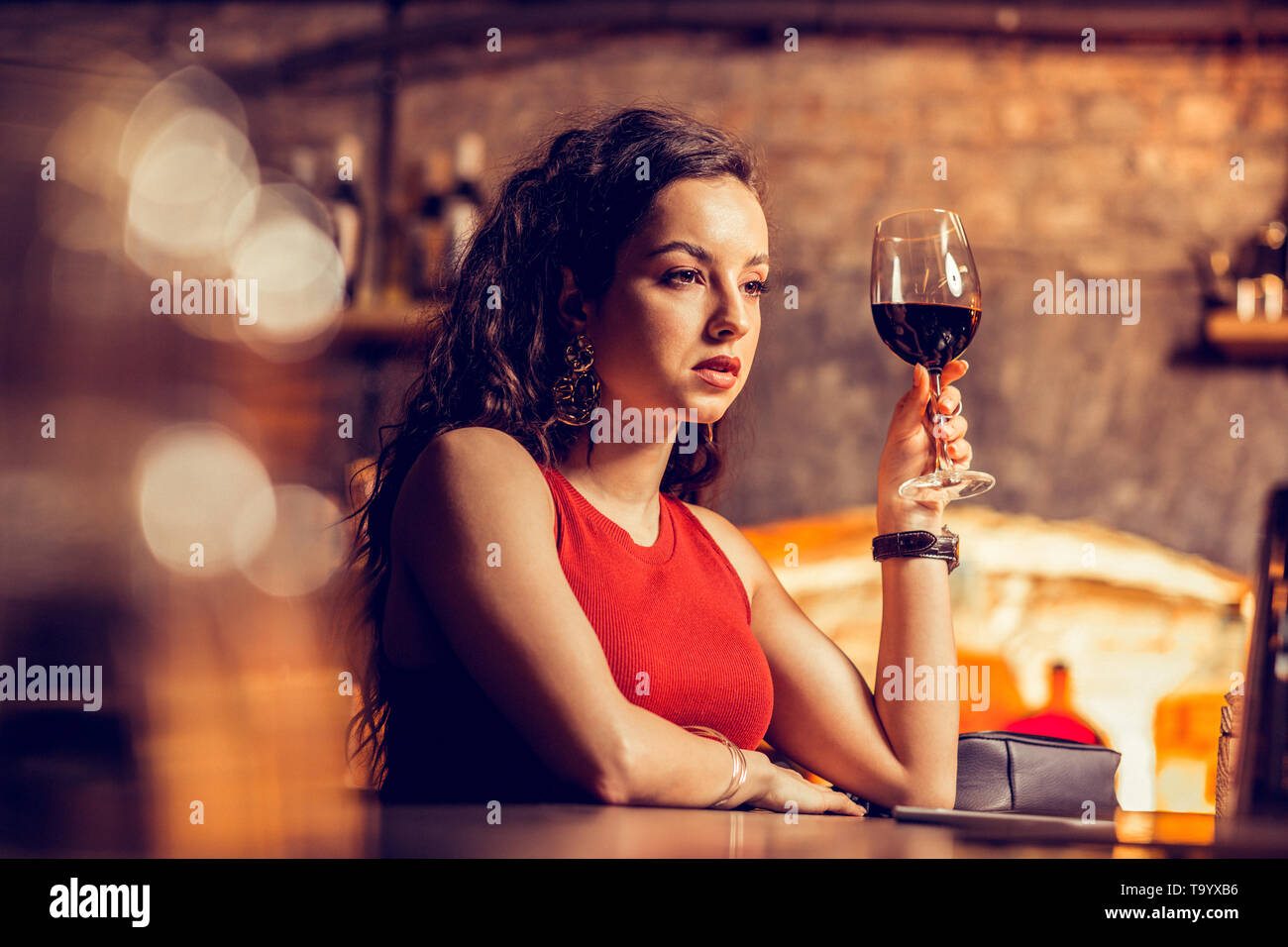 Curly woman sitting at bar counter and drinking wine Stock Photo